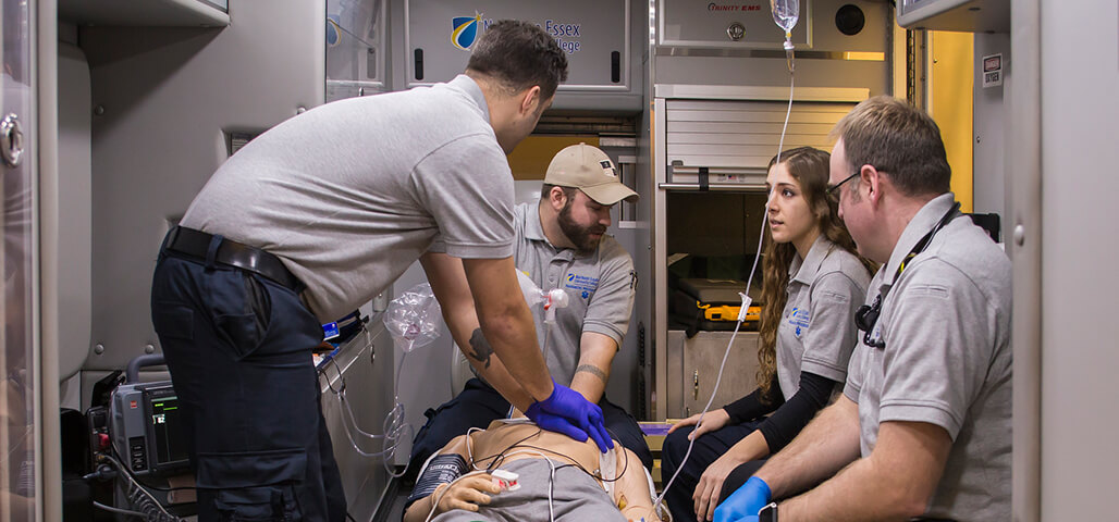 Four Paramedic Technology students working on a 'patient' in the ambulance simulation room, which is set up with equipment and technology like an ambulance.