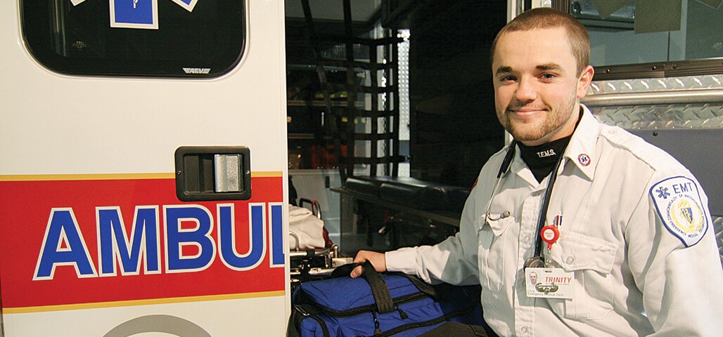 A Paramedic Technology  Assocaite degree student in EMT uniform, standing at the open door of a stocked ambulence.