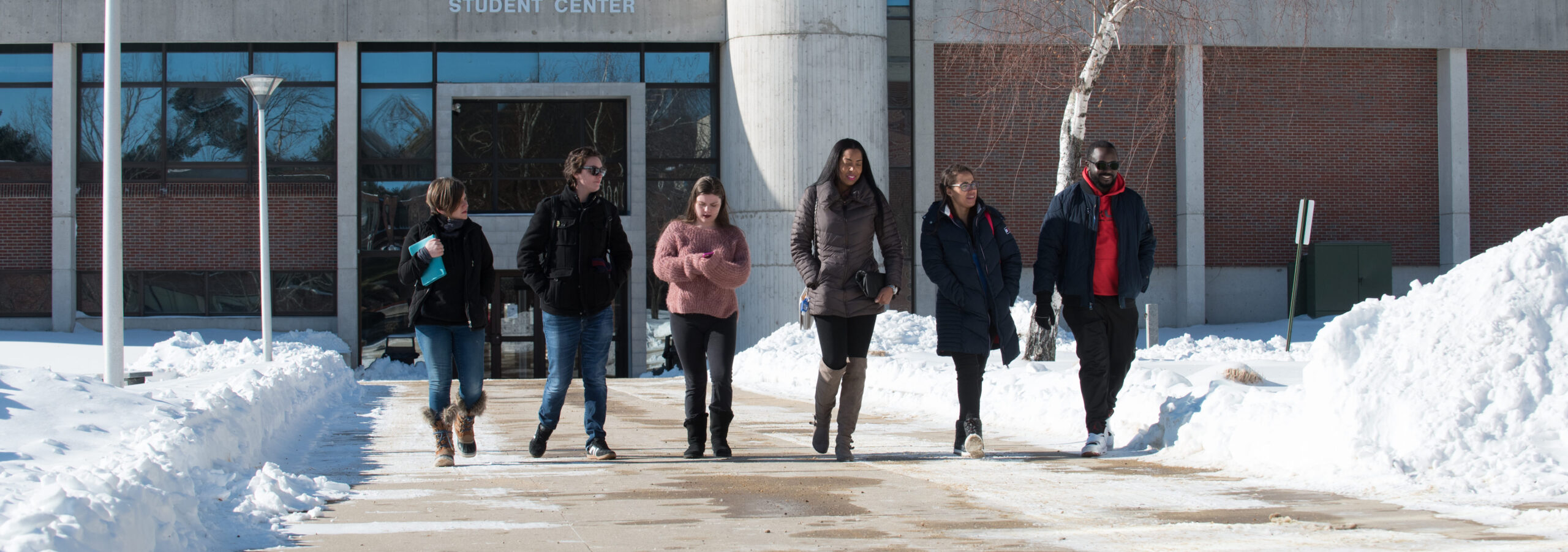 A photo of a group of students walking outside on the Haverhill campus, wearing winter jackets, walking with snow banks all around them through a cleared path