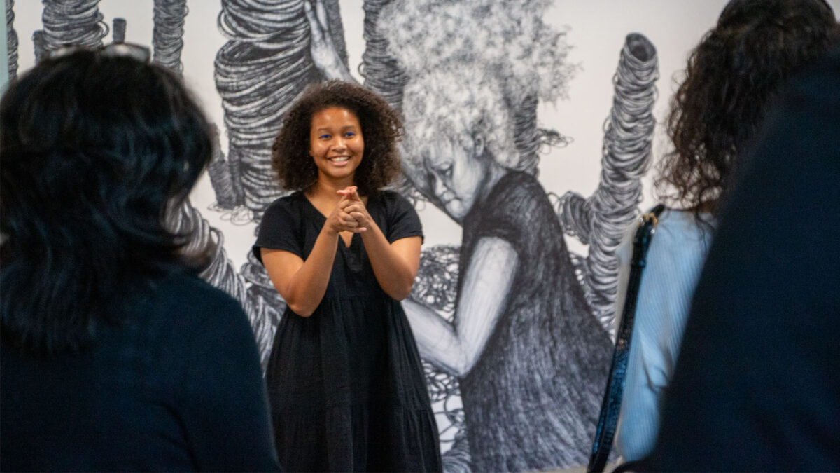 A woman in the ArtSpace holding her hands in excitement smiling in front of her art.